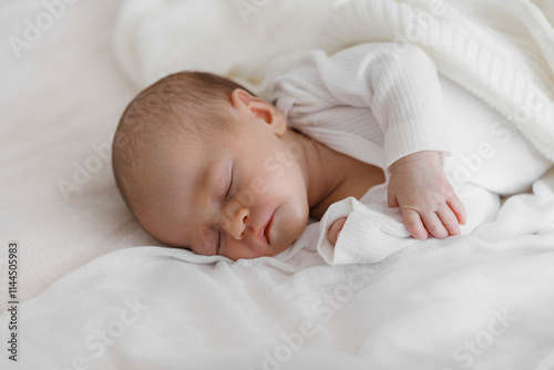 A baby is sleeping on a white blanket. The baby is wrapped in a blanket and has its head resting on its chest