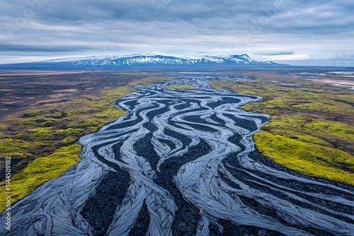 Aerial view of a braided river flowing through a vibrant green landscape, with mountains in the background.