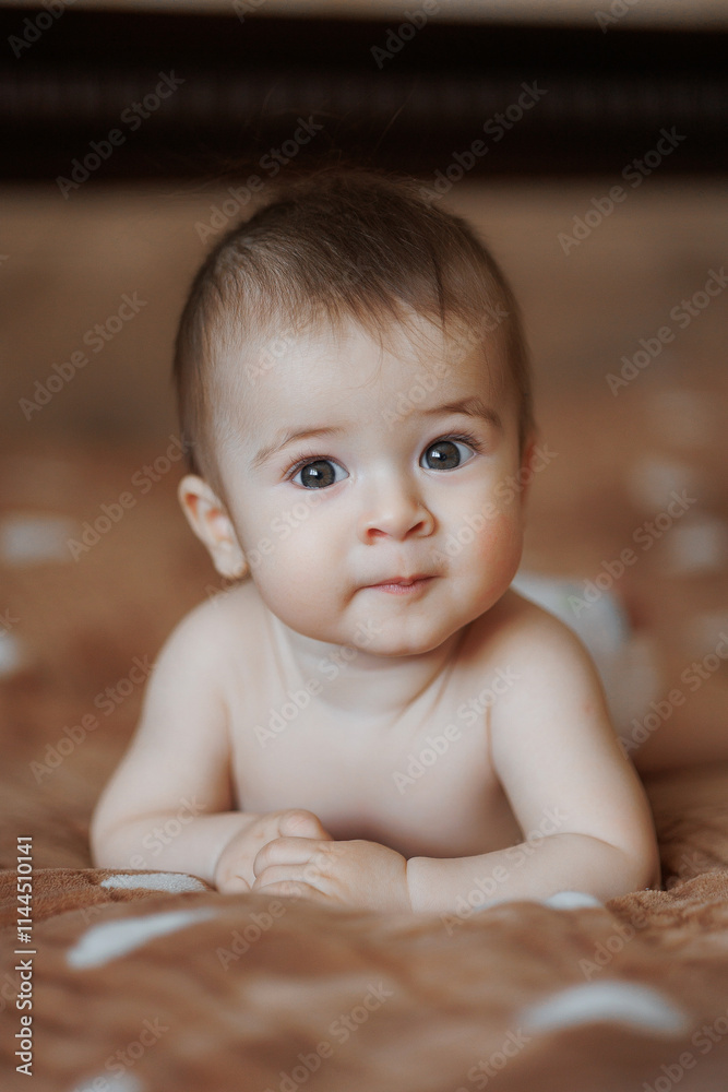 A baby is laying on a bed with its head tilted to the side. The baby's eyes are wide open, and it is looking at the camera. Concept of curiosity and innocence
