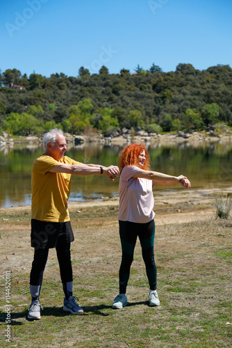 Senior couple stretching by the lake on sunny day