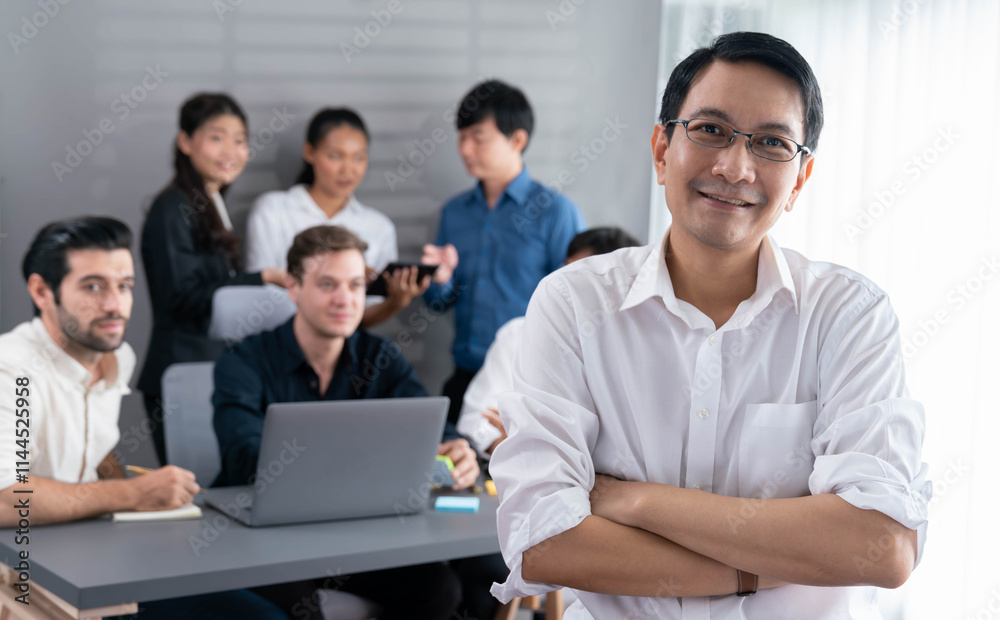 Confidence and happy smiling businessman portrait with background of his colleague and business team working in office. Office worker teamwork and positive workplace concept. Prudent Confidence and happy smiling businessman portrait with background of his colleague and business team working in office. Office worker teamwork and positive workplace concept. Prudent