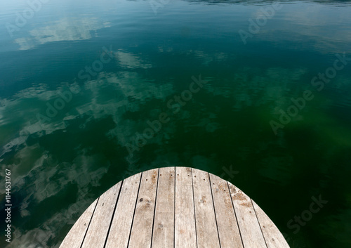 Sky and Clouds reflected in the clear green water of the lake. Old wooden pier in a green lagoon.