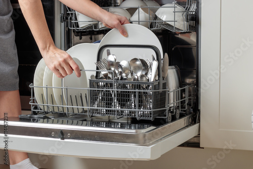 Female hand unloading dishwasher with tableware. Kitchen appliances, lifestyle view. Woman takes a plate from the dishwasher. Concept of modern technologies in the kitchen