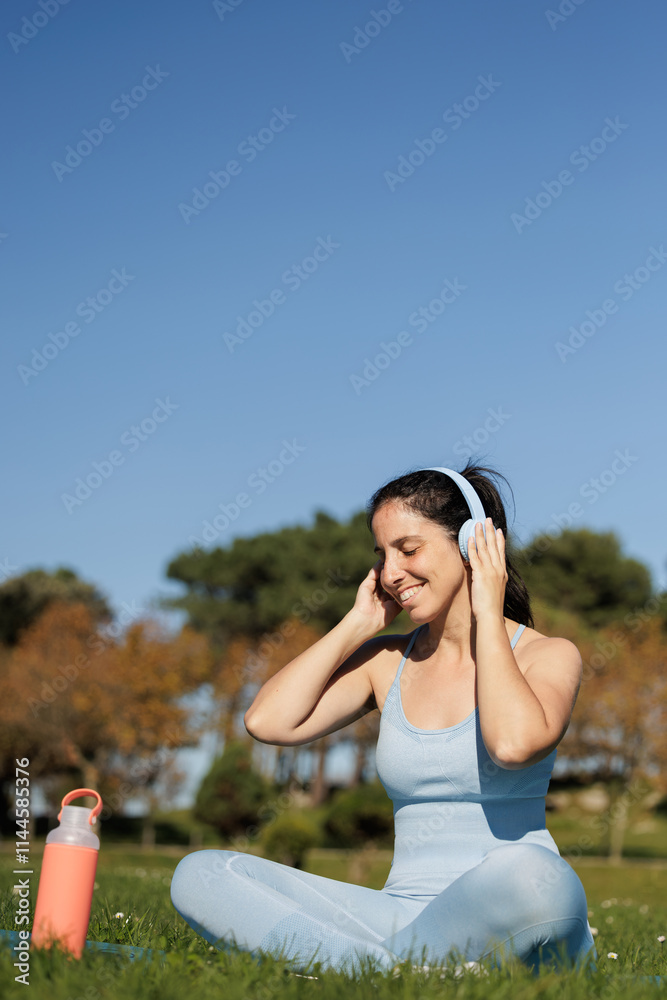 Happy and smiling young woman enjoys music in her headphones chosen from her smartphone, she does sports outdoors on a sunny day. Happy and smiling young woman enjoys music in her headphones chosen from her smartphone, she does sports outdoors on a sunny day.