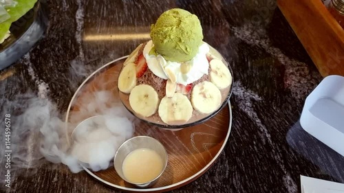 bingsu chocolate banana and red slice strawberry. matcha green tea ice cream decorative with whip cream with smoke dry ice. summer frozen cold condensed milk syrup.