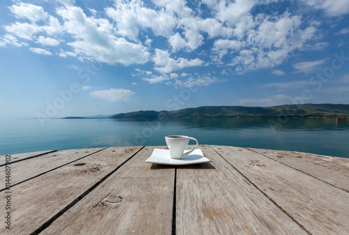 Cup of coffee on the wooden balcony and the morning lake with the blue sky