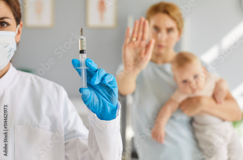 Anti-vaccine activism, mother proclaiming opposition to vaccination for newborn baby, stop immunization shot on childhood vaccine schedule in clinic by pediatrician doctor to protect small child  photo