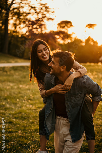 Happy couple having a piggyback ride in a beautiful park during sunset