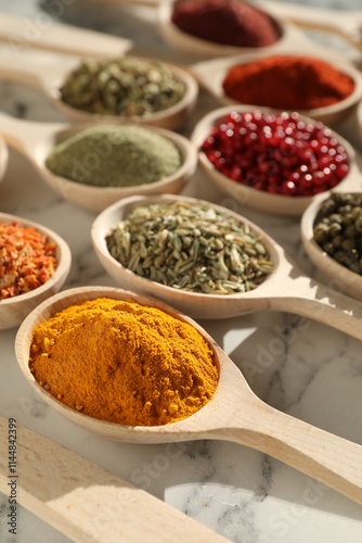 Different aromatic spices in spoons on white marble table, closeup