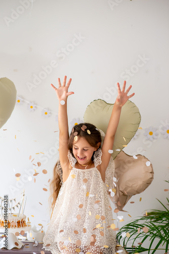 Little girl cheerfully celebrates her birthday. A portrait of a child throws up colorful tinsel and confetti. Positive emotions. Happy excited laughing child under sparkling confetti shower photo