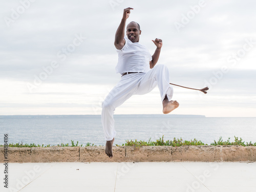 Capoeira martial artist jumping wearing white, alongside the ocean outdoors