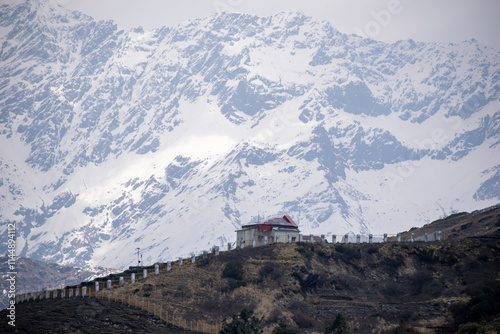 A serene landscape and high altitude observatory with red roof atop a rugged hill, surrounded by a fenced pathway.Towering snow covered mountains in the background, creates a breathtaking alpine view.