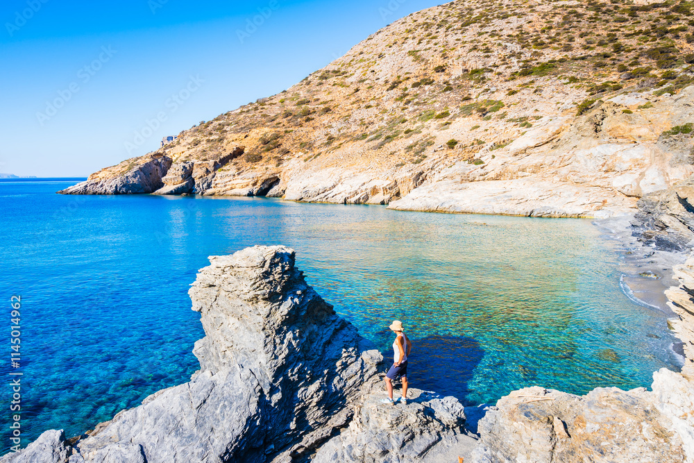 Woman tourist standing on rock and looking at blue sea in Mouros bay with amazing beach, Amorgos island, Cyclades, Greece