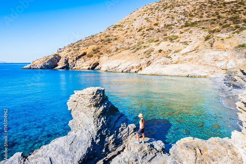 Obraz na płótnie Woman tourist standing on rock and looking at blue sea in Mouros bay with amazing beach, Amorgos island, Cyclades, Greece w salonie