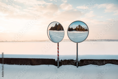 Two convex mirrors reflecting winter road. Snowy landscape in the background.
