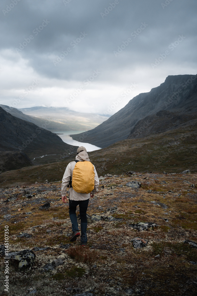 Hiker with a yellow rain cover trekking through a rugged Norwegian mountain valley Hiker with a yellow rain cover trekking through a rugged Norwegian mountain valley