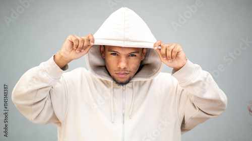 Man in beige hoodie looking serious with hands on hood