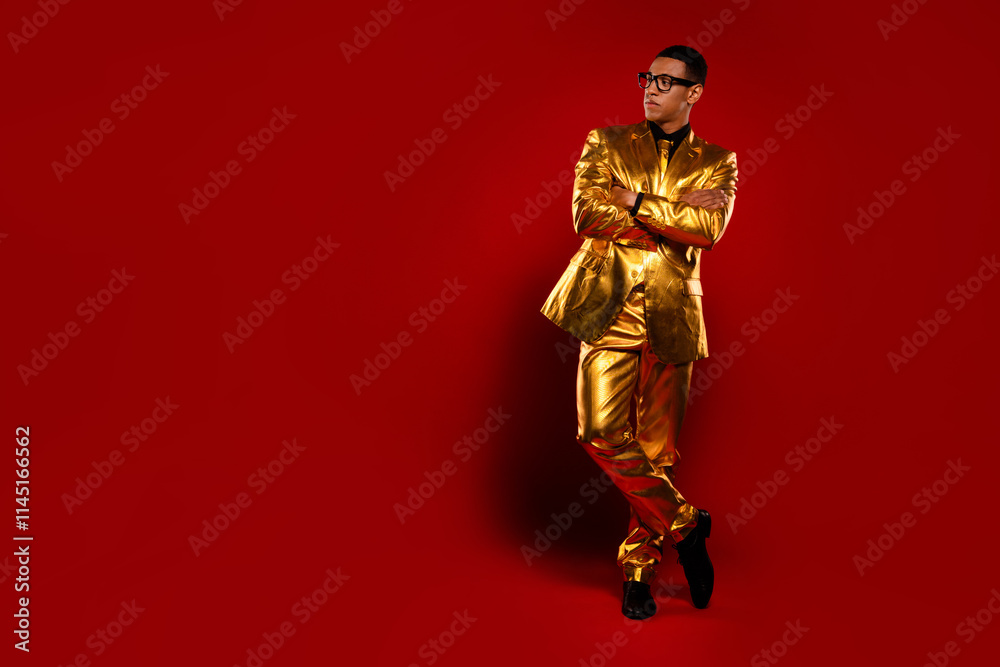 Elegant young man in glossy gold suit poses confidently against vibrant red background, wearing stylish sunglasses Elegant young man in glossy gold suit poses confidently against vibrant red background, wearing stylish sunglasses