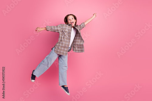 Tableau sur toile Cheerful young girl jumping against a pink background wearing a checkered shirt