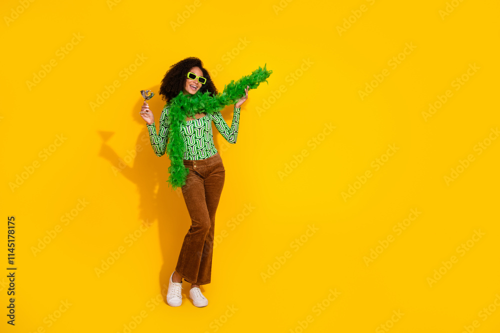 Young woman with black curly hair in vibrant fashion clothes holding a cocktail on a yellow background, exuding joy and charm Young woman with black curly hair in vibrant fashion clothes holding a cocktail on a yellow background, exuding joy and charm