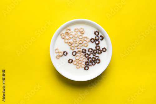 A mix of chocolate and plain cheerios floating in milk in a plain white bowl on a yellow background