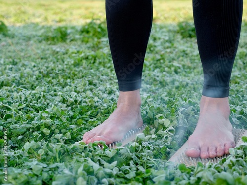 A barefoot woman stands on nails sadha board among the grass. Spiritual practice meditation in nature. Close-up