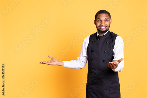 Smiling friendly butler pointing direction to left or right sides against yellow background, creating an advertisement for the catering industry. Five star restaurant employee.
