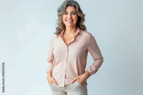 Half-length portrait of a woman in her 50s looking into the camera and wearing a casual blouse and trousers, standing against a solid-colored background