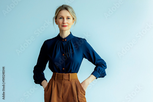 Half-length portrait of a woman in her 50s looking into the camera and wearing a casual blouse and trousers, standing against a solid-colored background