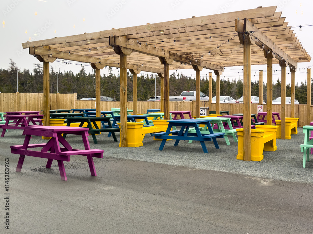 custom made wallpaper toronto digitalA beer garden with multiple wooden picnic tables under a wooden shelter for sun protection. The benches and tables are painted colorful and bright paint. The backyard garden is enclosed with a fence.