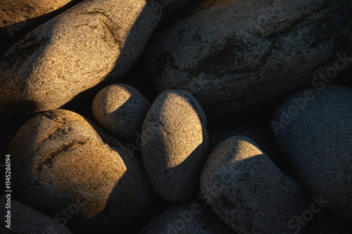 Smooth egg-shaped cobblestone boulders lit by the golden setting sun on a beach in Acadia National Park, Maine