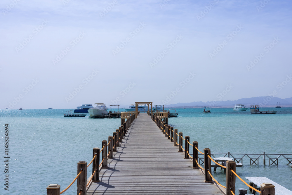 Obraz premium Serene pier overlooking turquoise sea with boats on a clear day