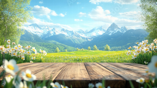 Spring background with a wooden table top, green grass, and white flowers in front of the spring mountains with snow on the peaks