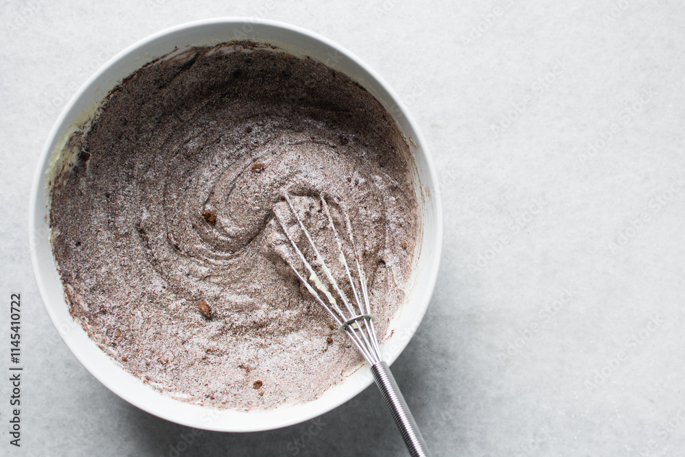Fototapeta premium Overhead view of red velvet cake batter being mixed in a white ceramic bowl, Red velvet cake batter in white ceramic mixing bowl, process of making red velvet cake