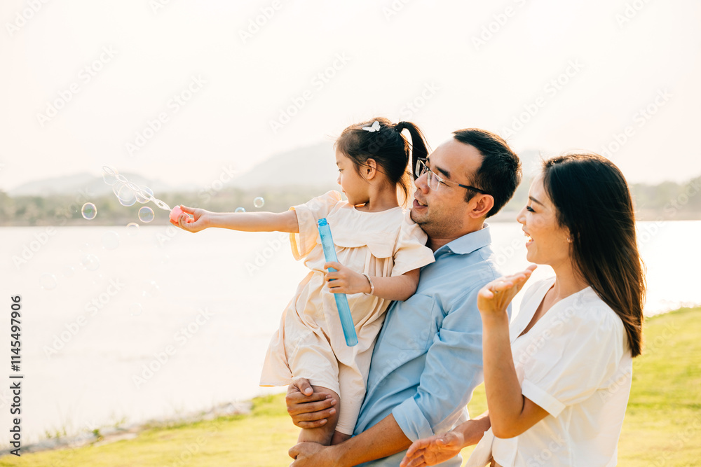 Asian family having fun playing together on spring meadow field grass in park, Happy parents father carrying daughter and a child blowing soap bubbles enjoying outdoors together with mother Asian family having fun playing together on spring meadow field grass in park, Happy parents father carrying daughter and a child blowing soap bubbles enjoying outdoors together with mother