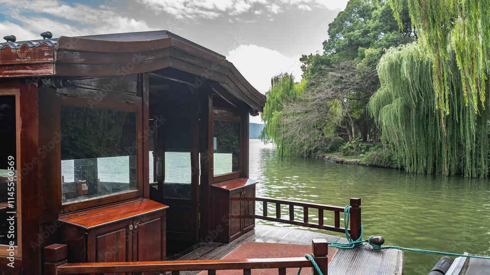 Beautiful Chinese tourist boat. A fragment. Wooden railings, cupboards, curved roof. The mooring ropes are stretched. There is lush green vegetation on the shore. Willow bent over the water. China. Beautiful Chinese tourist boat. A fragment. Wooden railings, cupboards, curved roof. The mooring ropes are stretched. There is lush green vegetation on the shore. Willow bent over the water. China.
