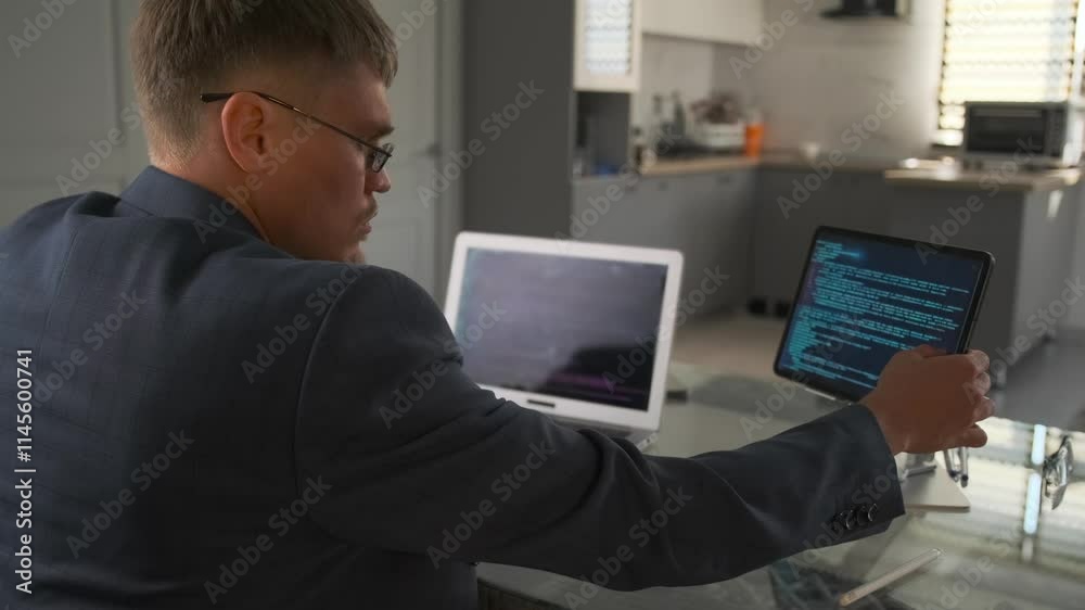 Developer in suit reviews code on laptop in minimalist living room. Developer in suit reviews code on laptop in minimalist living room.