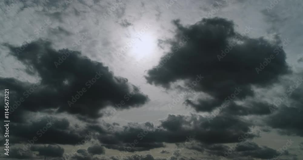 Timelapse of the overcast sky with the sun softly shining through light grey altostratus clouds and contrasting dark cumulus clouds moving fast and changing shapes