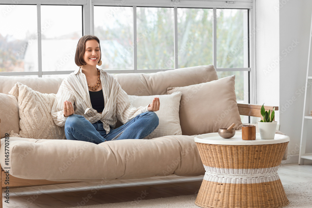 Beautiful young woman meditating on sofa at home Beautiful young woman meditating on sofa at home