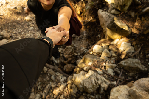 Male hiker helping a woman to climb a rocky path in the mountains, copy space