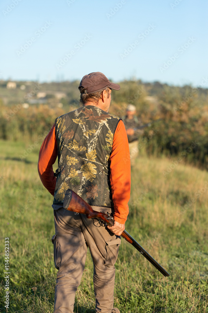 Mature hunter man holding a shotgun and walking through a field Mature hunter man holding a shotgun and walking through a field