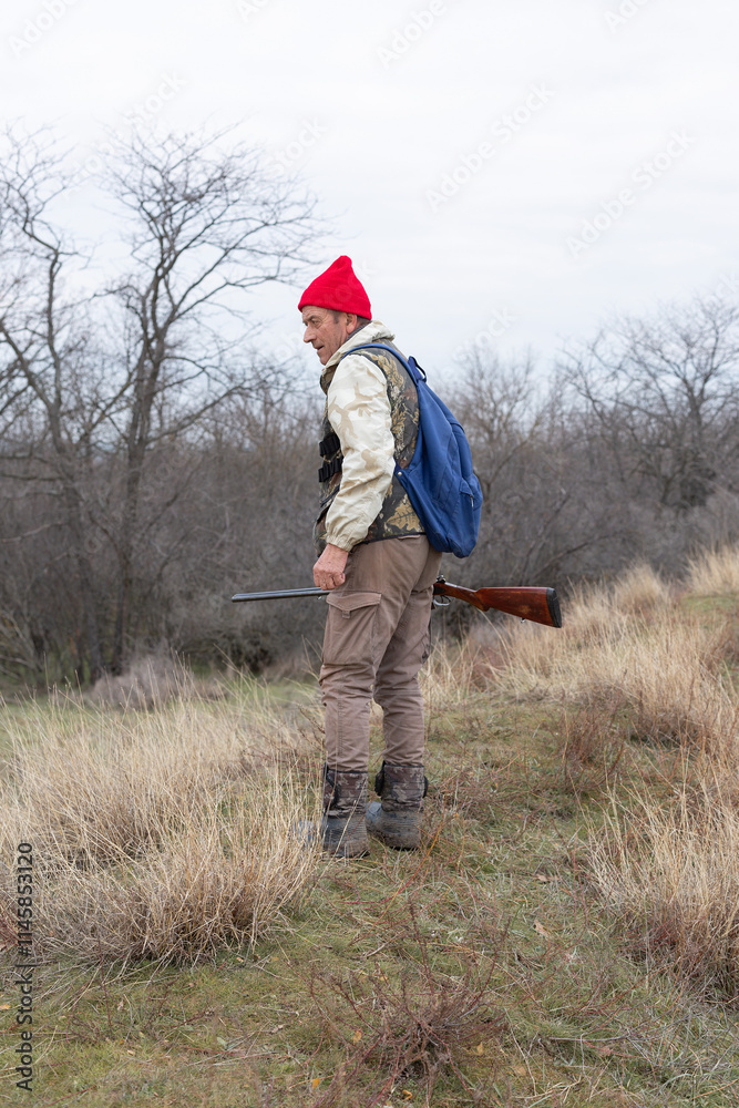 Mature hunter man holding a shotgun and walking through a field Mature hunter man holding a shotgun and walking through a field
