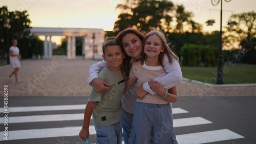 Portrait of a happy family brunette girl her little daughter and son posing and smiling standing near a pedestrian crossing in the park in the evening in summer