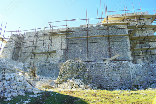 The process of restoring an ancient fortification: a high defensive wall with scaffolding installed along it. Restoration of the medieval fortress of Herceg Stjepan in Ljubuski, Bosnia and Herzegovina photo