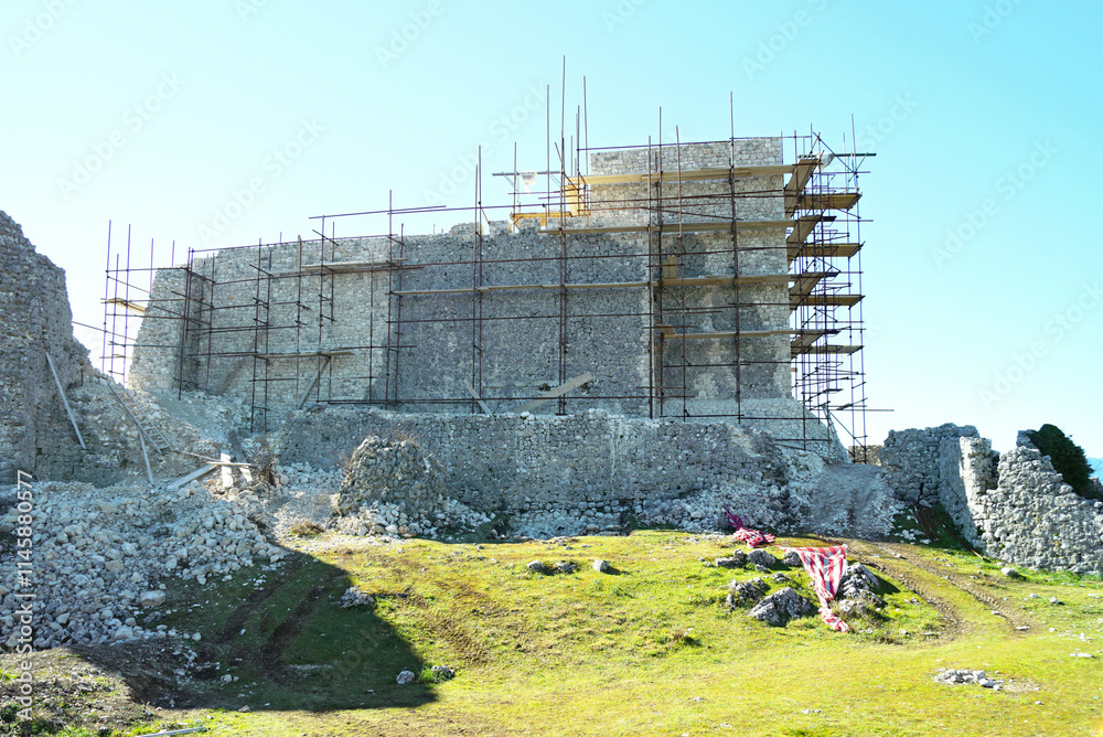 Φωτογραφία Restoration of a historical monument: a landscape with destroyed buildings, construction debris and a medieval citadel with scaffolding installed along its walls (Ljubuski, Bosnia and Herzegovina)