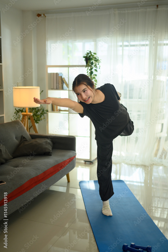 Young asian woman practicing yoga in living room balancing on one leg while extending her arm forward Young asian woman practicing yoga in living room balancing on one leg while extending her arm forward