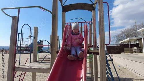 Little girl having fun on outdoor playground. Playing on slide