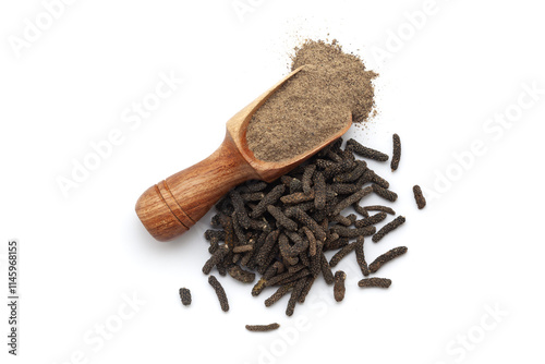 A wooden scoop filled with organic long pepper (Piper longum) powder, placed beside a heap of long pepper fruits, isolated on a white background. photo