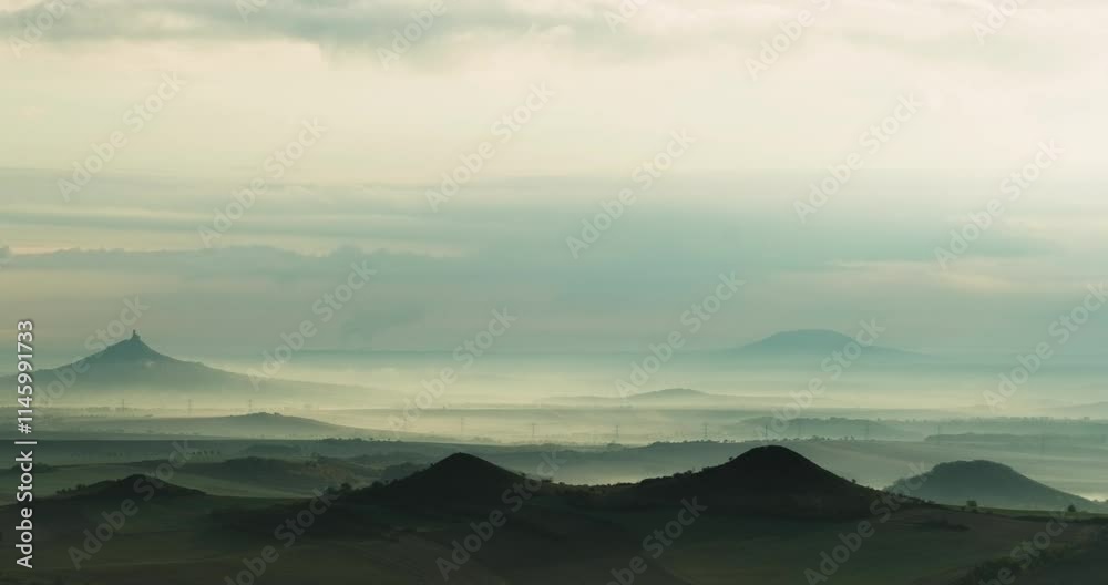 Timelapse of hilly landscape with a silhouette of castle ruins on one hillwith mist rolling in valleys and shadows transforming with time and of overcast sky white and grey clouds on a cloudy day Timelapse of hilly landscape with a silhouette of castle ruins on one hillwith mist rolling in valleys and shadows transforming with time and of overcast sky white and grey clouds on a cloudy day