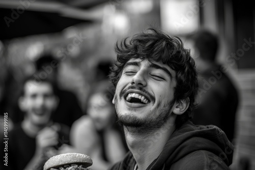 A joyous young man is caught in a candid moment, laughing vividly while holding a delicious burger, expressing happiness and casual enjoyment in social setting. photo